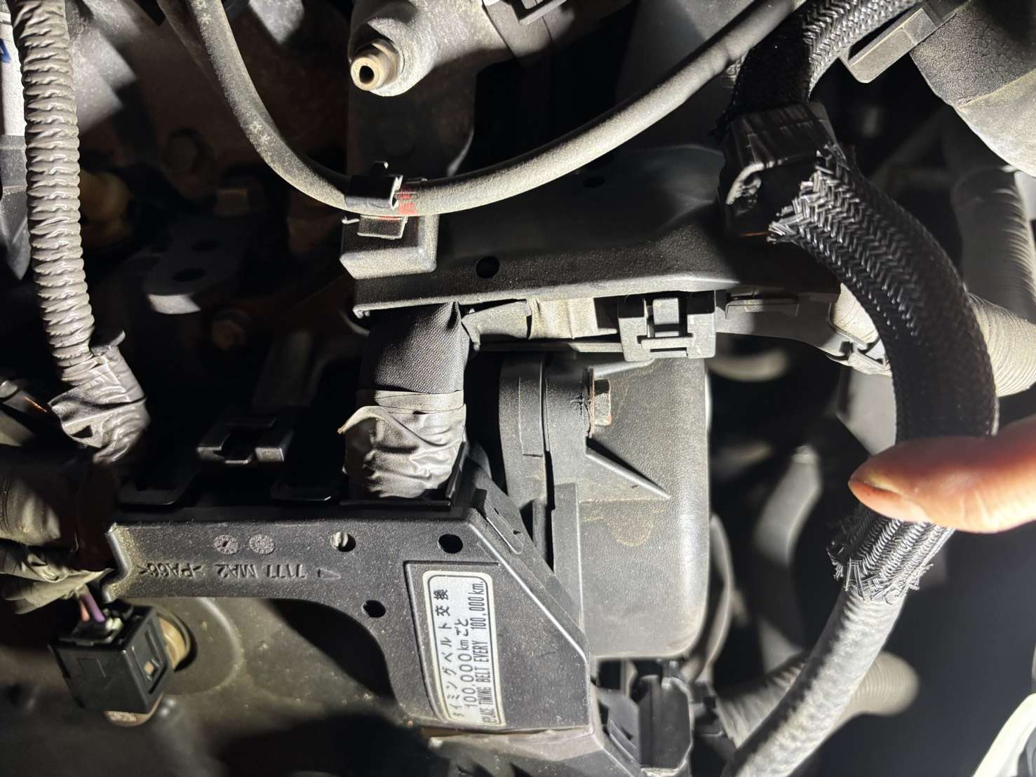ハイエース1KDのタイミングベルトカバー手前のハーネスとクランプ部分を指さしているところ