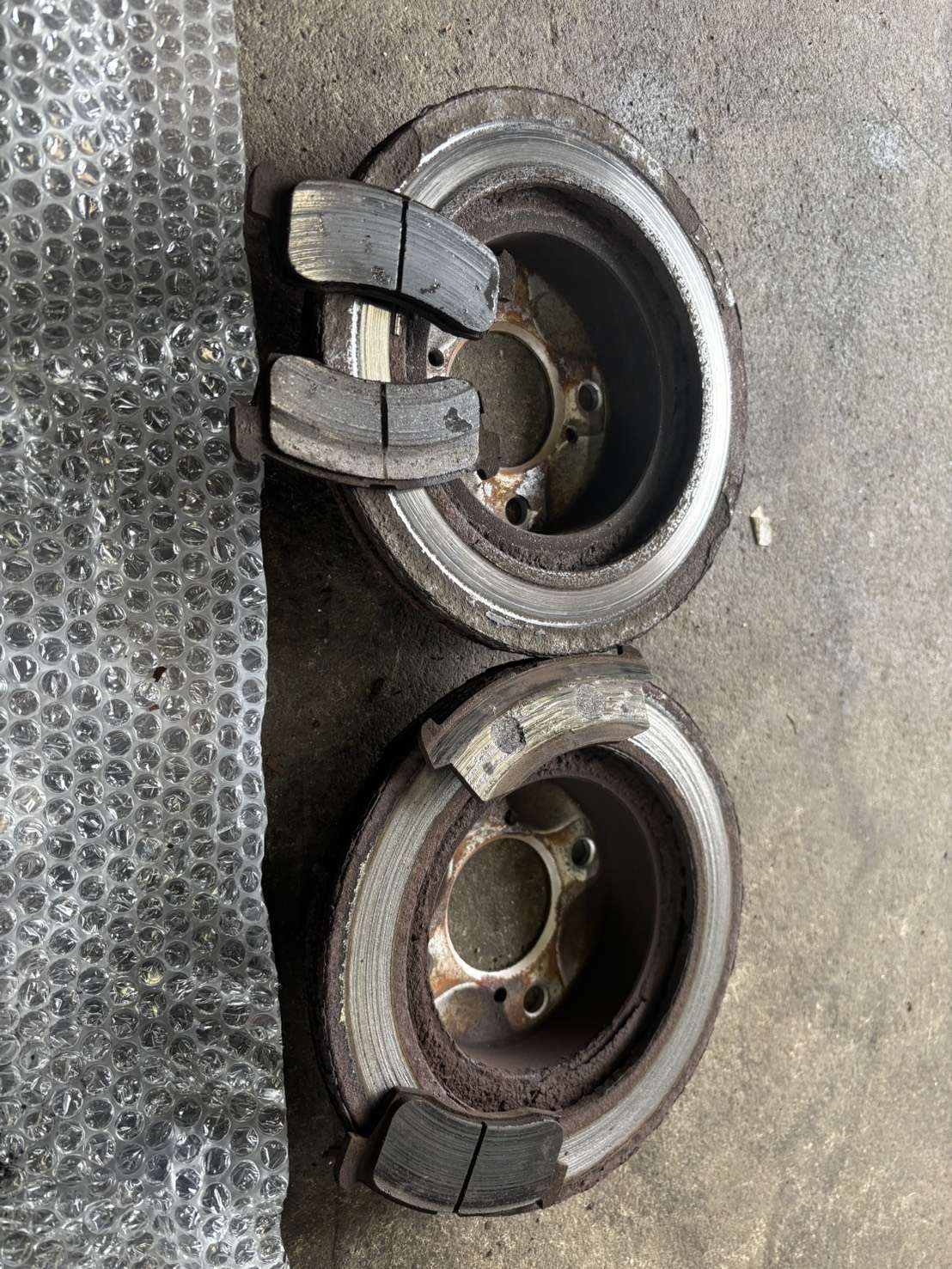 スペーシアMK32Sから外した古いフロントブレーキローター2枚と古いブレーキパッド。パッドの摩擦材は残っておらず、ローターの外周には段ができている